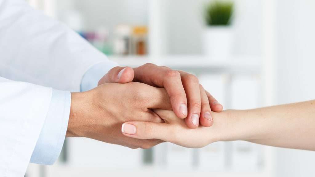 Dr. Tashko’s visual of personalized endocrine care showing a compassionate physician gently holding a patient’s hand in a bright, clinical setting. The close-up gesture symbolizes empathy, trust, and the human connection essential to individualized treatment. The background features a softly blurred medical office, reinforcing a calm, supportive, and patient-centered approach to care.